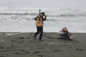 Woman tumbling onto soft sand with guitar held high.